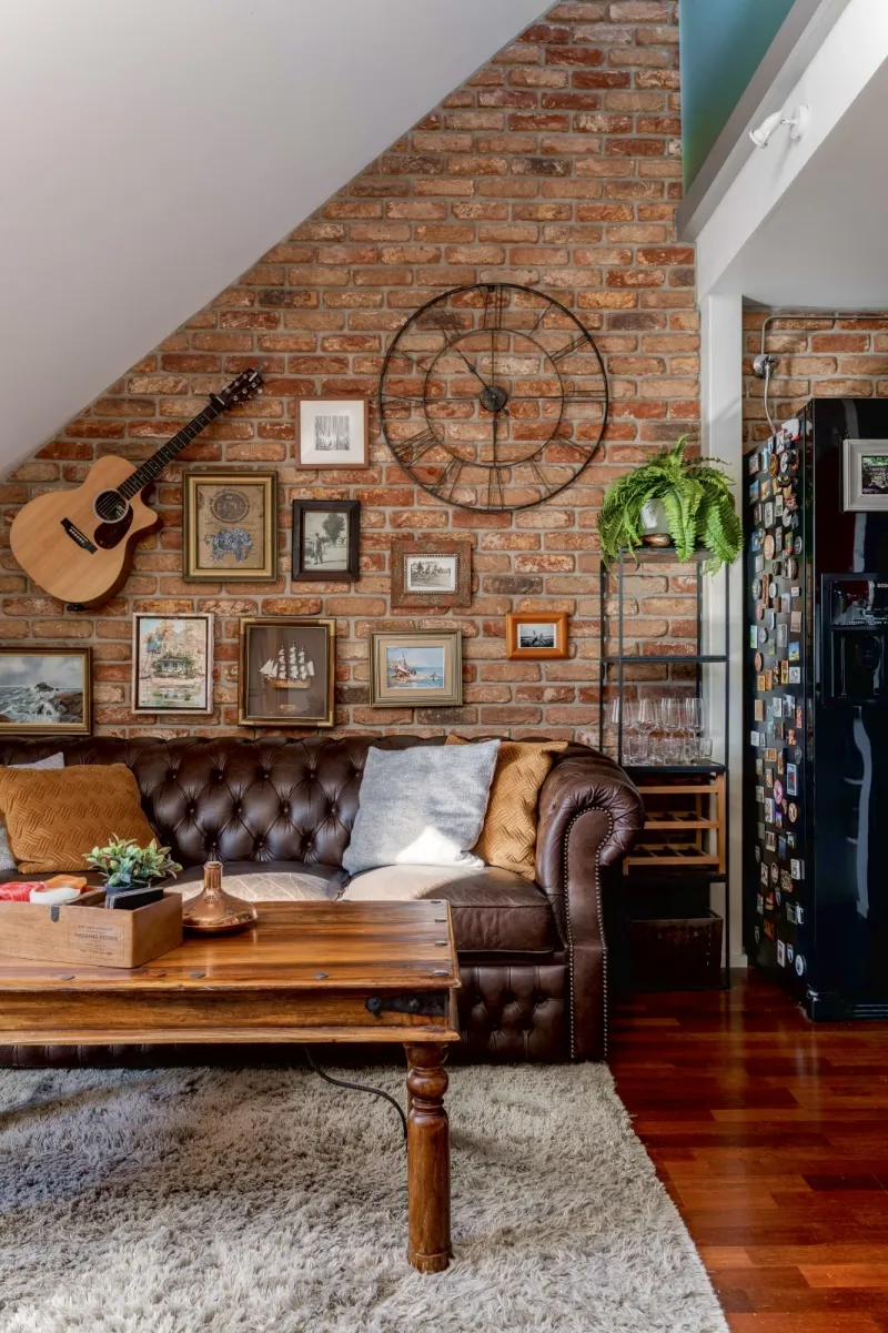 Gallery wall of small maritime paintings and a guitar on exposed brick above the Chesterfield