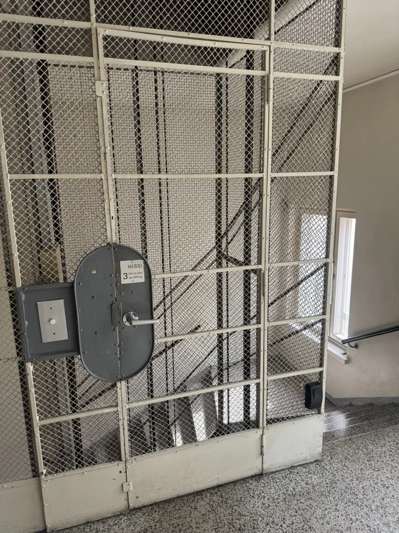 The lift shaft on the eighth-floor landing, with a black lock box mounted on the mesh