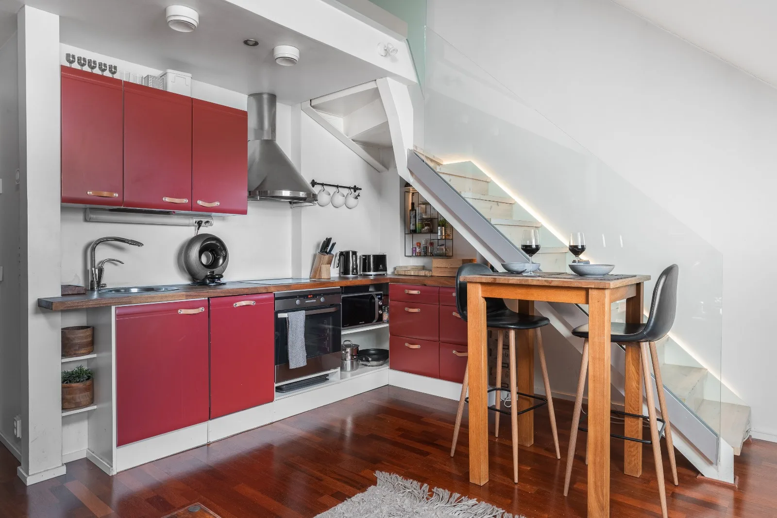 Crimson kitchen with butcher-block counter, induction hob and oven, beside a tall oak table with two stools