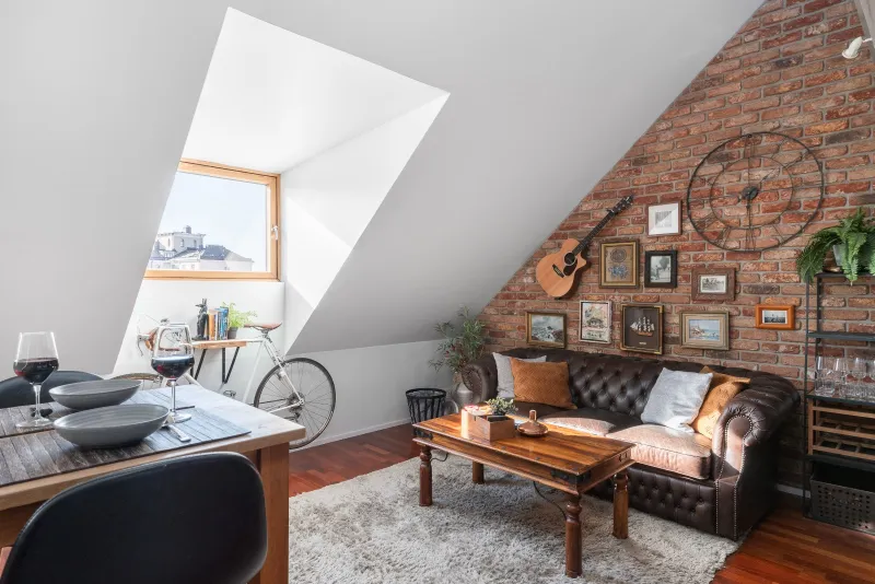Living room with dining table, bicycle under the roof window and brick wall