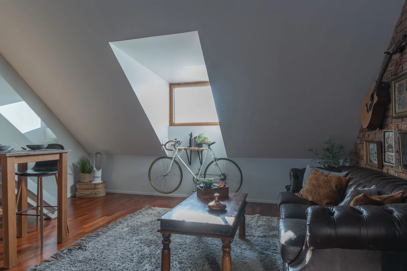 Living room under the sloped ceiling with a deep roof-window recess, a road bike parked beneath it and a leather Chesterfield sofa
